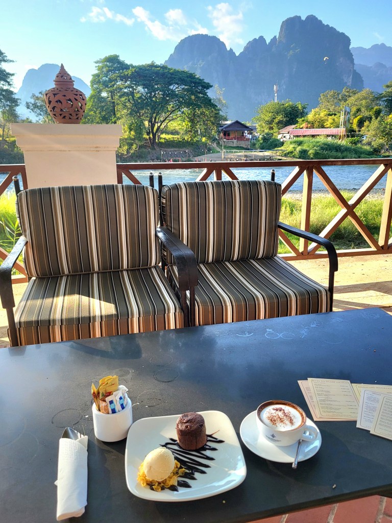 Un café en terrasse avec un fond de montagnes, un dessert au chocolat et une boule de glace sur une table.